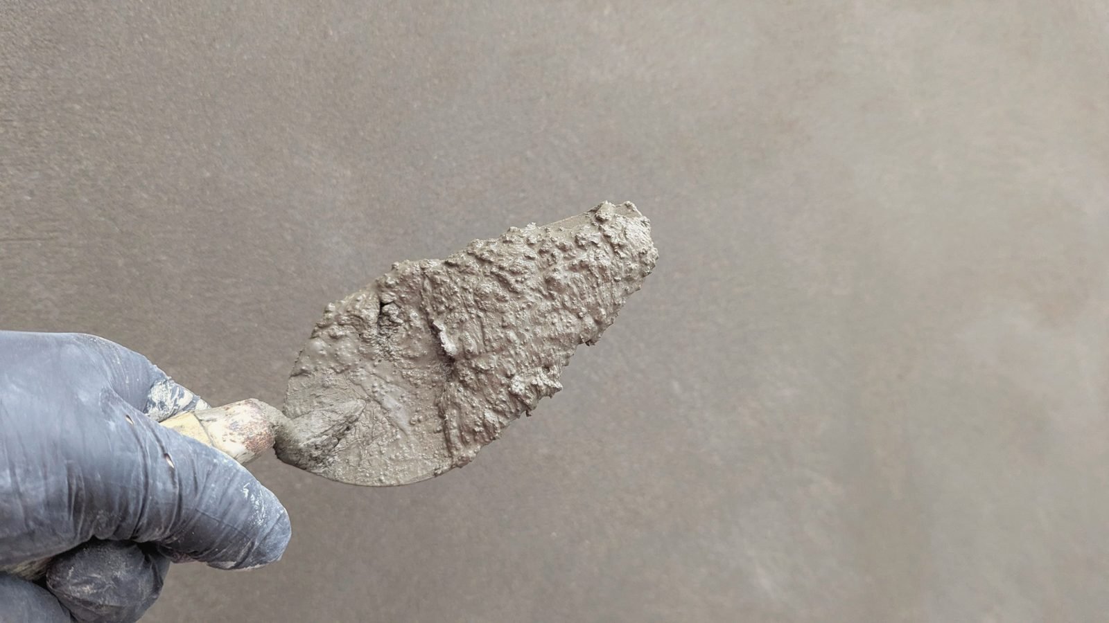 Fresh cement lifted on a trowel, held before a smoothed wall.